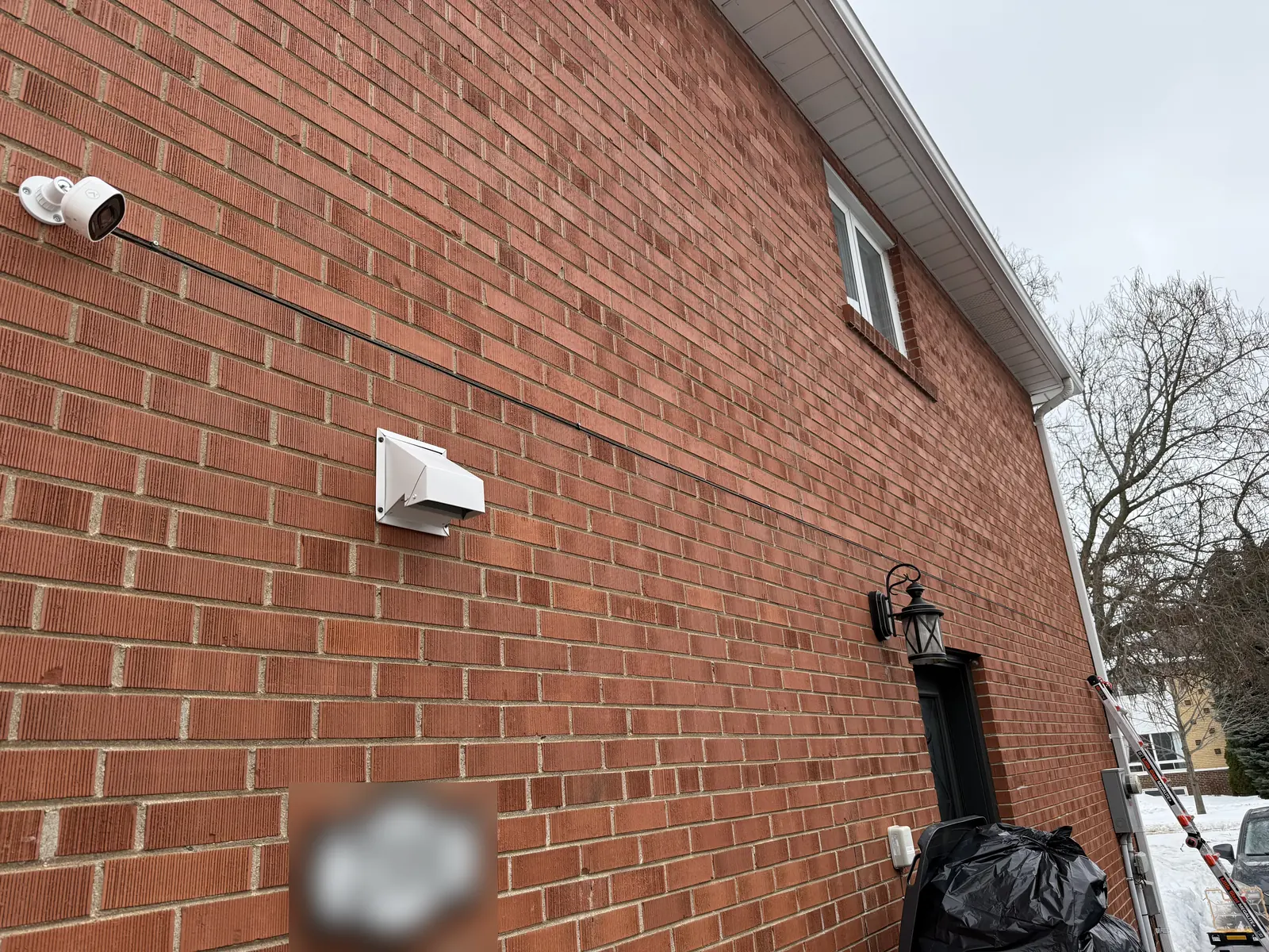 Exterior bullet camera mounted high on the brick side wall of a house